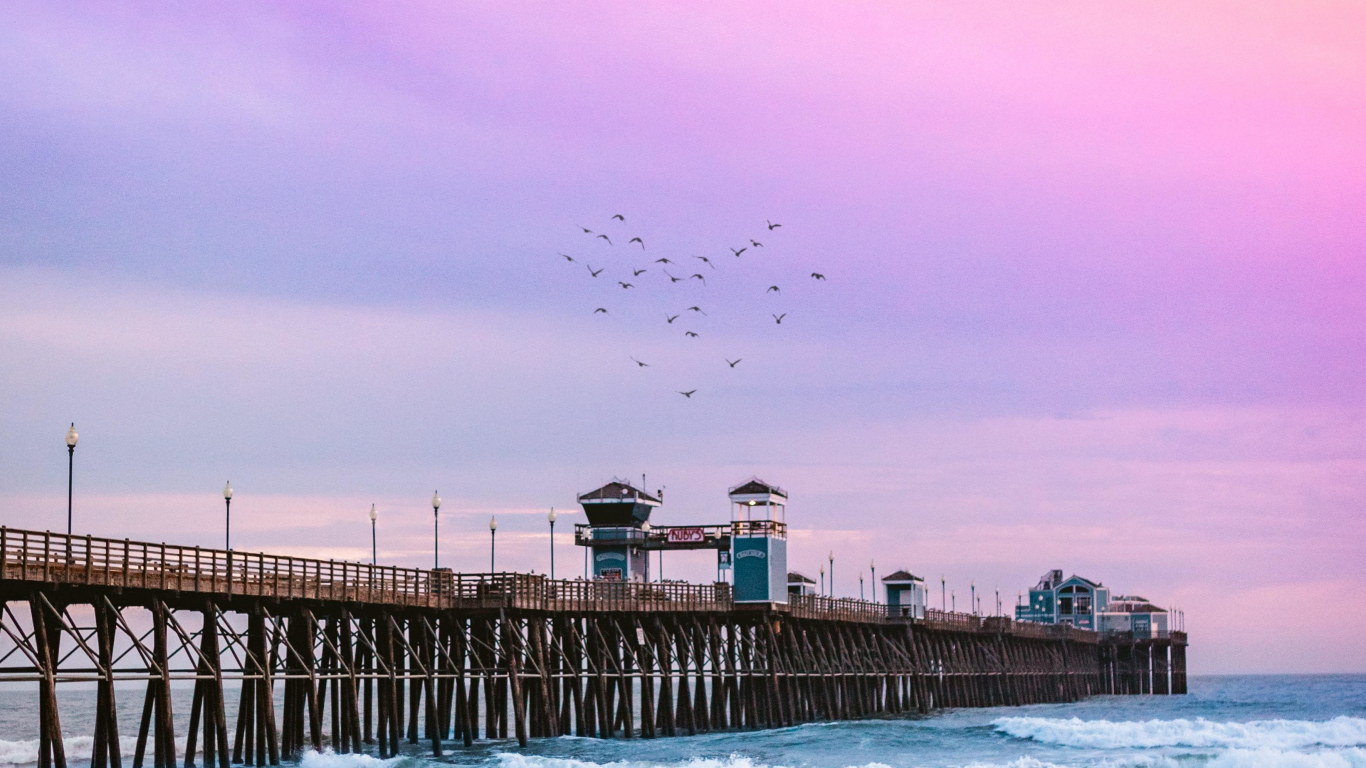 Download wallpaper 1366x768 pier, calm beach, pink sky, sunset